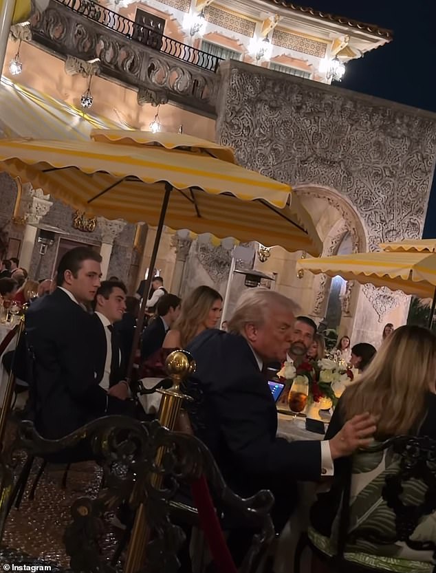 Un tímido barón Trump se mantiene reservado mientras se sienta junto a su padre en una cena festiva en Mar-a-Lago.