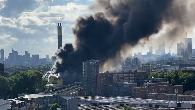 Alrededor de 100 bomberos luchan contra un gran incendio en un centro de reciclaje mientras una espesa columna de humo se eleva sobre el horizonte de Londres.