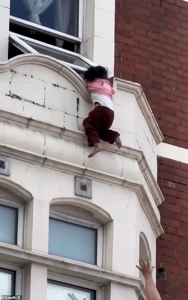 El momento en que una joven se aferra al borde de una ventana encima de una tienda de Londres antes de caer en manos de un hombre y un oficial de policía debajo
