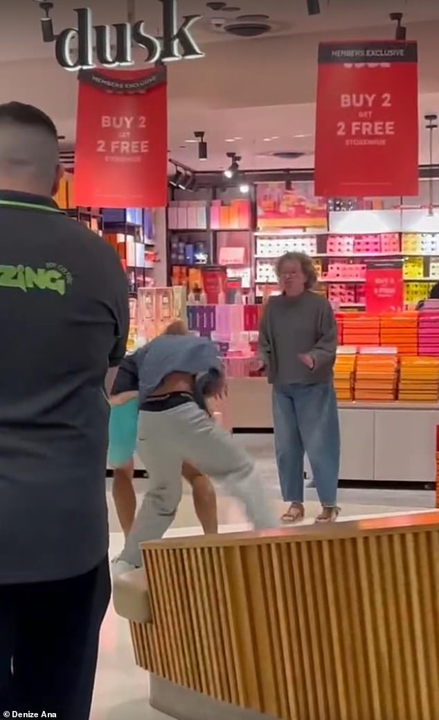 Una mujer de mediana edad interviene para poner fin a una violenta pelea entre dos jóvenes que se ha desatado frente a una tienda de velas aromáticas.