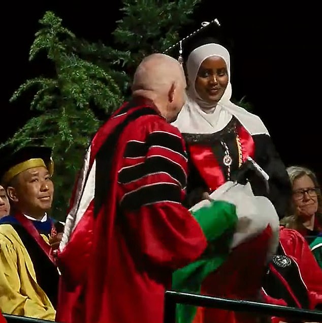 Momento en que el rector de la Universidad de Seattle toma las manos de un estudiante mientras se prepara para revelar la bandera palestina en la ceremonia de graduación.
