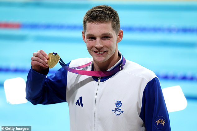 Holly, la esposa de Adam Ramsay-Peaty, observa cómo la estrella llega a la final de los 100 m braza después de un extraño retraso de 10 minutos en la clasificación, y el héroe local Duncan Scott se lleva el oro.
